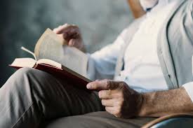 Personne âgée assise dans un fauteuil avec un livre ouvert. On ne voit pas son visage.